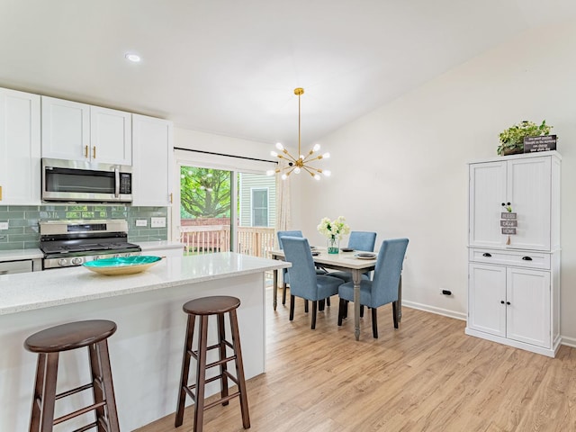 7559 Kingsbury Dr, Hanover Park, IL 60133 - kitchen featuring appliances with stainless steel finishes, light wood-style flooring, a kitchen breakfast bar, a chandelier, and white cabinetry