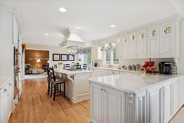 1219 N Lakeview Ct, Palatine, IL 60067 - kitchen with a kitchen bar, custom exhaust hood, light wood-style floors, white cabinets, and glass insert cabinets