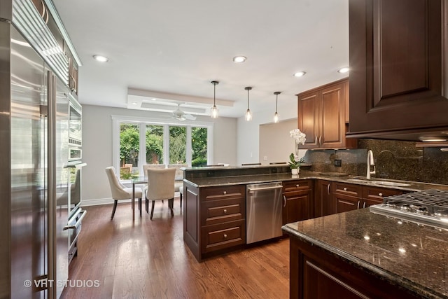 36 Logan Ter, Golf, IL 60029 - kitchen featuring appliances with stainless steel finishes, decorative backsplash, dark wood-style floors, a peninsula, and dark stone counters