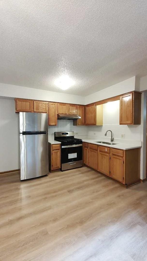 222 W 26th St Unit 202, Chicago, IL 60616 - kitchen featuring appliances with stainless steel finishes, a textured ceiling, light countertops, light wood-style floors, and brown cabinets