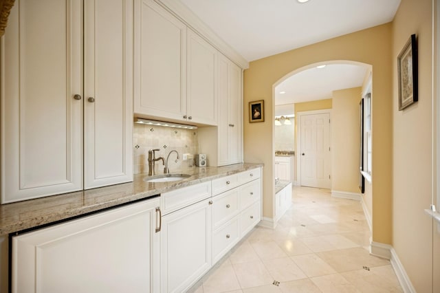 1054 Seneca Rd, Wilmette, IL 60091 - kitchen featuring arched walkways, decorative backsplash, light stone counters, white cabinets, and light tile patterned flooring