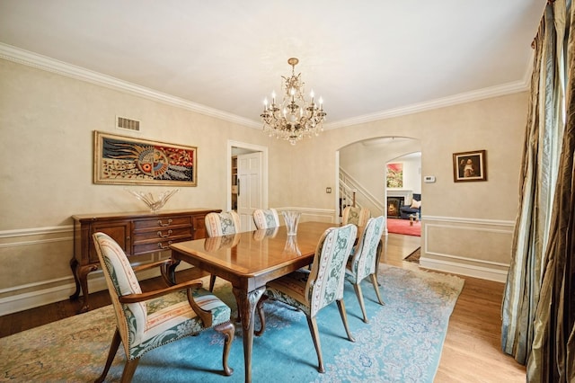1054 Seneca Rd, Wilmette, IL 60091 - dining space with arched walkways, light wood-type flooring, a chandelier, and crown molding
