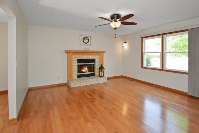 708 Wheeler Dr, Hudson, IL 61748 - unfurnished living room featuring light wood finished floors, ceiling fan, and a brick fireplace