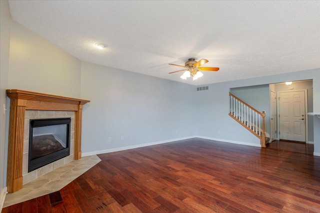 516 Wild Turkey Ln, Normal, IL 61761 - unfurnished living room with stairway, wood finished floors, a tiled fireplace, ceiling fan, and a textured ceiling
