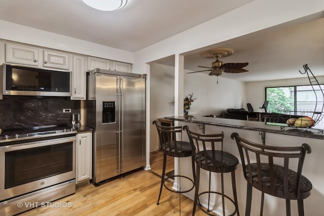 6229 N Niagara Ave Unit 209, Chicago, IL 60631 - kitchen featuring appliances with stainless steel finishes, a breakfast bar area, light wood finished floors, a ceiling fan, and dark countertops