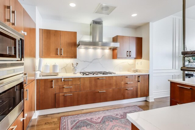 401 N Wabash Ave Unit 35J, Chicago, IL 60611 - kitchen featuring wall chimney range hood, stainless steel appliances, wood finished floors, brown cabinets, and light countertops