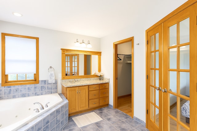 1102 Brian Dr, Manteno, IL 60950 - bathroom featuring french doors, vanity, a jetted tub, a spacious closet, and tile patterned floors