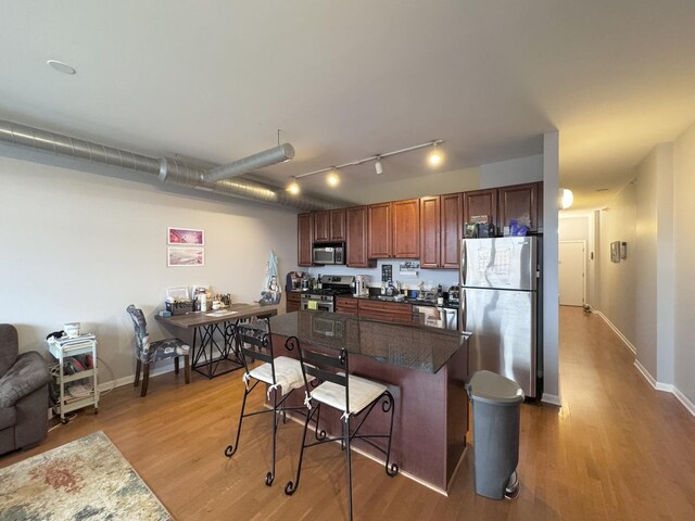 1200 W Monroe St Unit 516, Chicago, IL 60607 - kitchen with appliances with stainless steel finishes, a kitchen breakfast bar, light wood-style floors, dark countertops, and brown cabinets