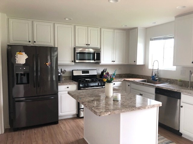 900 Heartland Park Ln, Antioch, IL 60002 - kitchen with appliances with stainless steel finishes, white cabinets, a kitchen island, light wood finished floors, and light stone countertops