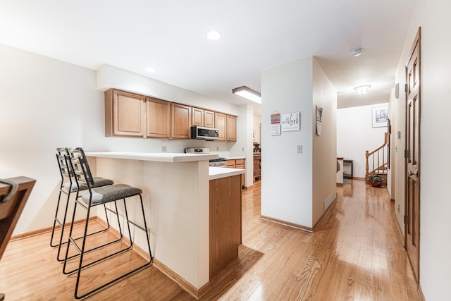 4 Meadow Trl W, Dekalb, IL 60115 - kitchen with stainless steel microwave, stove, a breakfast bar, light wood finished floors, and a peninsula