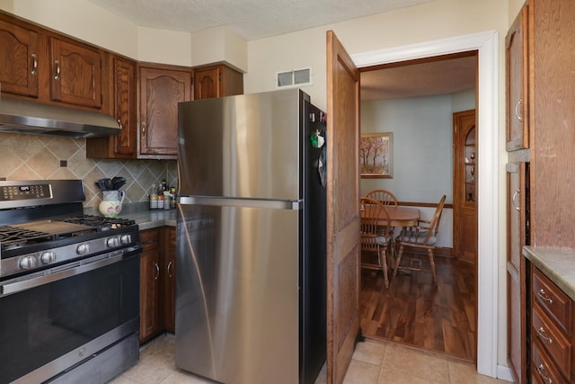1211 Hovey Ave, Normal, IL 61761 - kitchen with appliances with stainless steel finishes, under cabinet range hood, decorative backsplash, light tile patterned flooring, and brown cabinetry