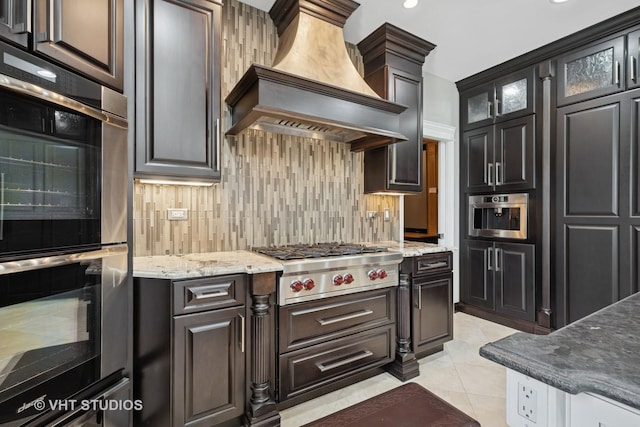 22 Westlake Dr, South Barrington, IL 60010 - kitchen featuring custom range hood, stainless steel appliances, tasteful backsplash, light stone counters, and glass insert cabinets