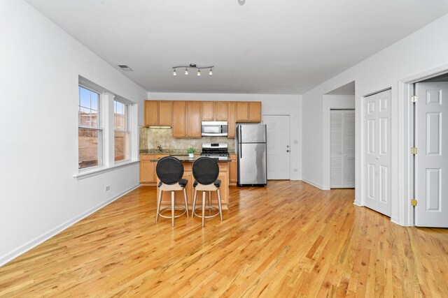 2414 W Bryn Mawr Ave Unit 1W, Chicago, IL 60659 - kitchen featuring appliances with stainless steel finishes, light wood-type flooring, a center island, and decorative backsplash