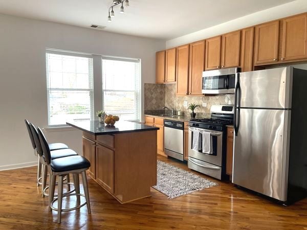 2414 W Bryn Mawr Ave Unit 1W, Chicago, IL 60659 - kitchen featuring appliances with stainless steel finishes, dark countertops, backsplash, dark wood-style floors, and a center island