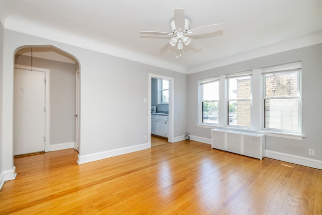 6751 N Artesian Ave Unit 2C, Chicago, IL 60645 - spare room with radiator heating unit, arched walkways, ceiling fan, and light wood finished floors