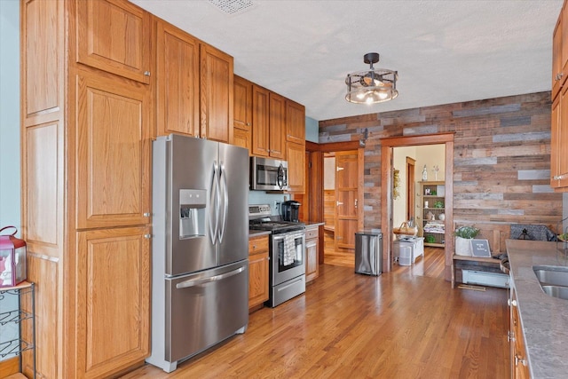 887 N 1100e Rd, Melvin, IL 60952 - kitchen featuring appliances with stainless steel finishes, light wood-style floors, wooden walls, brown cabinetry, and a textured ceiling