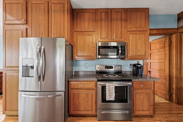 887 N 1100e Rd, Melvin, IL 60952 - kitchen with appliances with stainless steel finishes, light wood-style floors, brown cabinetry, dark countertops, and a textured ceiling