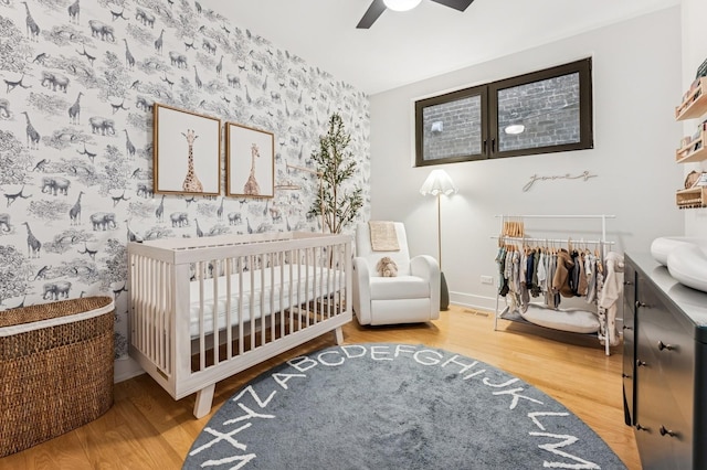 1423 W Huron St Unit 1, Chicago, IL 60642 - bedroom featuring wallpapered walls, wood finished floors, an accent wall, a crib, and a ceiling fan