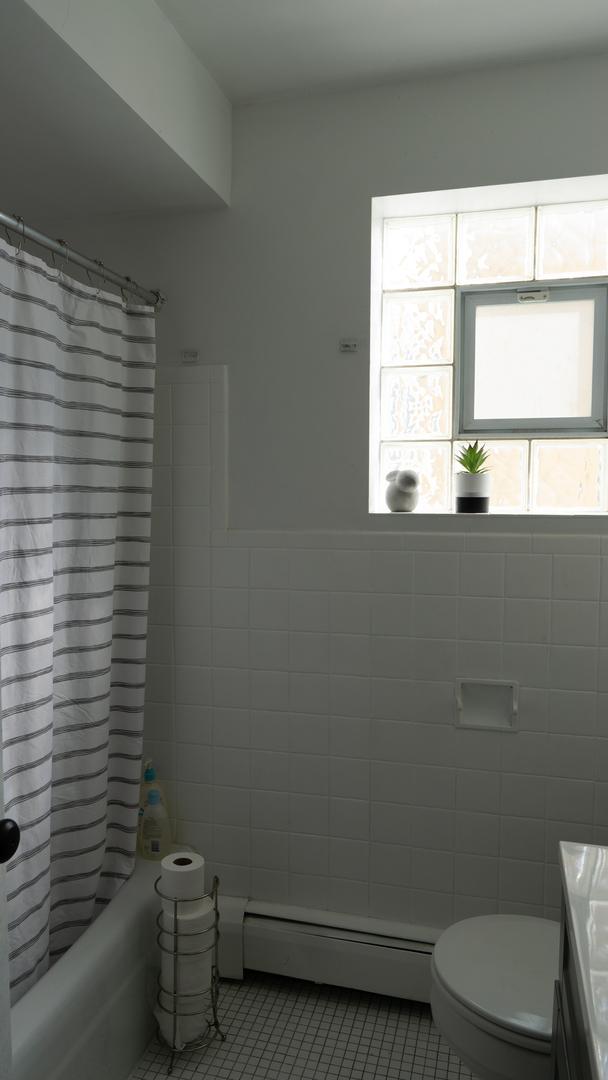 5704 W Montrose Ave Unit 2B, Chicago, IL 60634 - bathroom featuring baseboard heating, vanity, tile patterned flooring, tile walls, and shower / bath combo