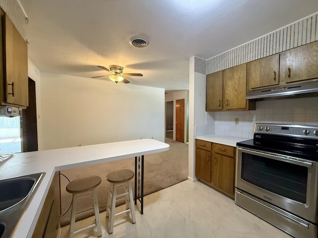 1340 Jeffrey Dr, Rantoul, IL 61866 - kitchen with stainless steel electric range, under cabinet range hood, brown cabinetry, decorative backsplash, and a ceiling fan