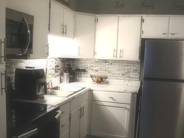 kitchen featuring freestanding refrigerator, stainless steel microwave, light countertops, tasteful backsplash, and white cabinets