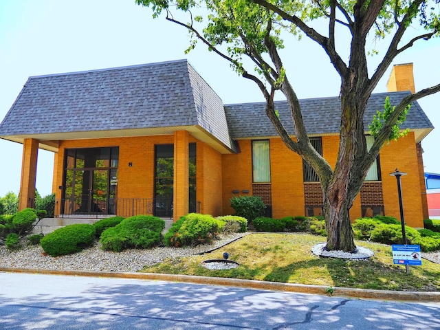 view of front of house featuring a shingled roof, brick siding, and mansard roof