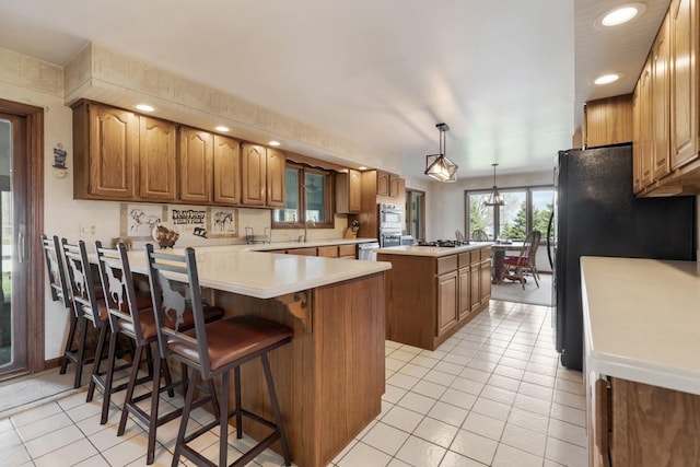 41W072 Bowes Rd, Elgin, IL 60124 - kitchen with a center island, light tile patterned flooring, freestanding refrigerator, brown cabinets, and a peninsula