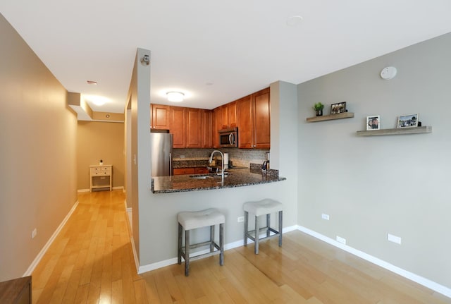 345 N La Salle Dr Unit 1010, Chicago, IL 60654 - kitchen featuring appliances with stainless steel finishes, light wood-style floors, decorative backsplash, a kitchen breakfast bar, and dark stone counters