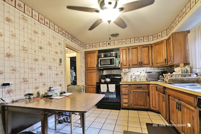 1247 Cavell Ave, Highland Park, IL 60035 - kitchen featuring black range with electric cooktop, stainless steel microwave, brown cabinets, light tile patterned floors, and wallpapered walls