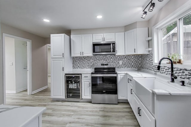 43173 N Lake Ave, Antioch, IL 60002 - kitchen featuring stainless steel appliances, wine cooler, white cabinetry, backsplash, and light wood-style floors