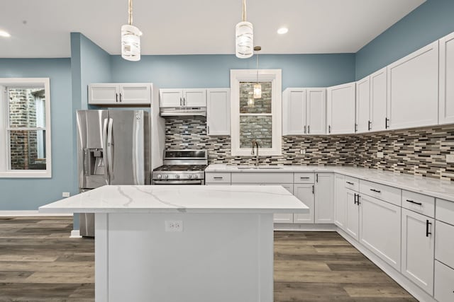 4025 W Adams St, Chicago, IL 60624 - kitchen featuring appliances with stainless steel finishes, under cabinet range hood, decorative backsplash, a center island, and dark wood-style flooring