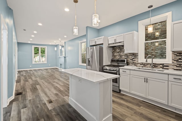 4025 W Adams St, Chicago, IL 60624 - kitchen featuring appliances with stainless steel finishes, under cabinet range hood, decorative backsplash, light stone counters, and decorative light fixtures