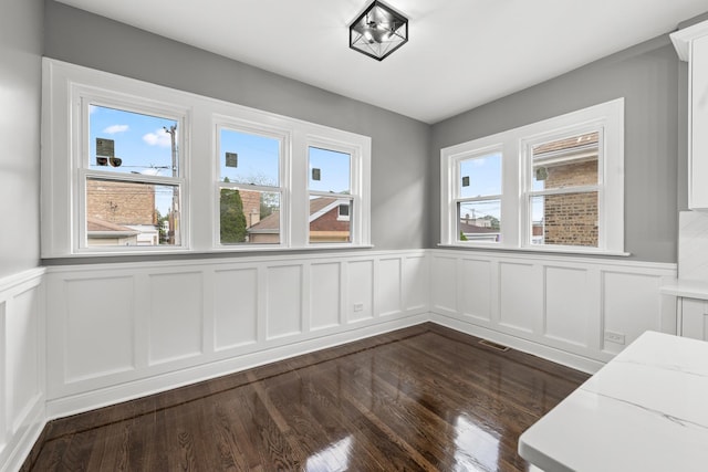 2107 E Ave, Berwyn, IL 60402 - unfurnished dining area featuring dark wood-style floors, healthy amount of natural light, a decorative wall, and a wainscoted wall