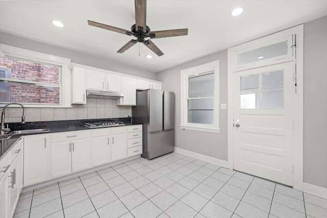 kitchen with appliances with stainless steel finishes, under cabinet range hood, backsplash, ceiling fan, and dark countertops