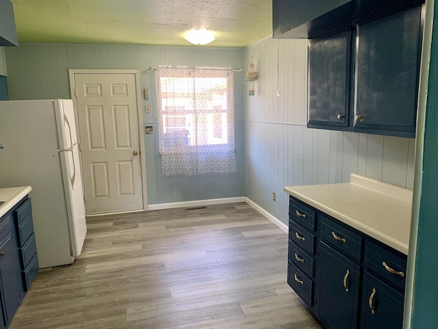 3122 Arlington Dr, Princeton, IL 61356 - kitchen featuring freestanding refrigerator, blue cabinetry, light countertops, light wood-style flooring, and a textured ceiling
