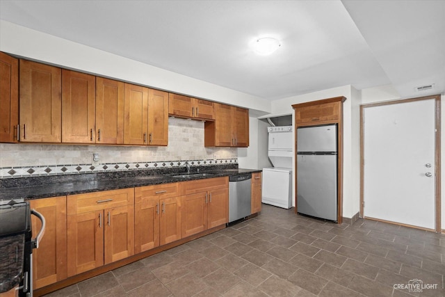 2301 Bicentennial Ave Unit 5, Crest Hill, IL 60403 - kitchen with stainless steel appliances, estacked washer and dryer, decorative backsplash, brown cabinets, and dark stone counters