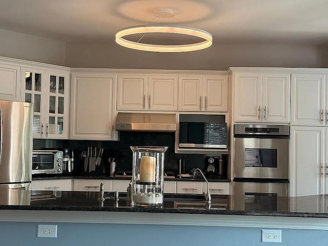 06N274 W Ridgewood Ln, Saint Charles, IL 60175 - kitchen featuring under cabinet range hood, appliances with stainless steel finishes, white cabinetry, glass insert cabinets, and dark stone countertops