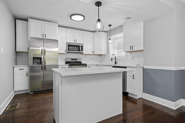 8051 S Paxton Ave, Chicago, IL 60617 - kitchen featuring appliances with stainless steel finishes, dark wood-style flooring, backsplash, white cabinets, and a kitchen island
