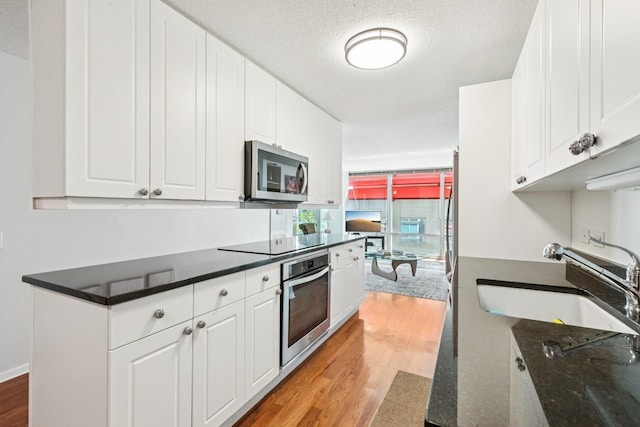 800 Elgin Rd Unit 1017, Evanston, IL 60201 - kitchen with appliances with stainless steel finishes, light wood-type flooring, white cabinets, a textured ceiling, and dark stone countertops