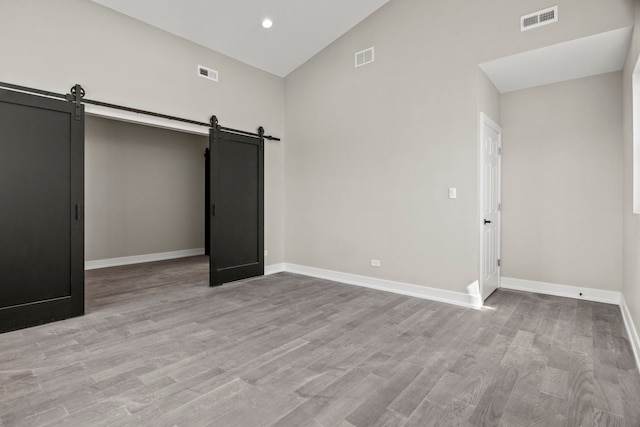 7711 S Ridgeland Ave, Chicago, IL 60649 - unfurnished bedroom with a barn door, high vaulted ceiling, light wood-style flooring, and recessed lighting