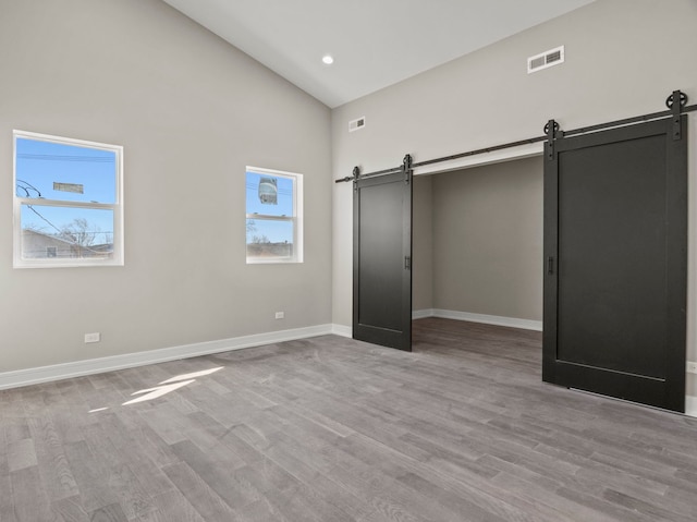 7711 S Ridgeland Ave, Chicago, IL 60649 - unfurnished bedroom with a barn door, high vaulted ceiling, wood finished floors, and recessed lighting