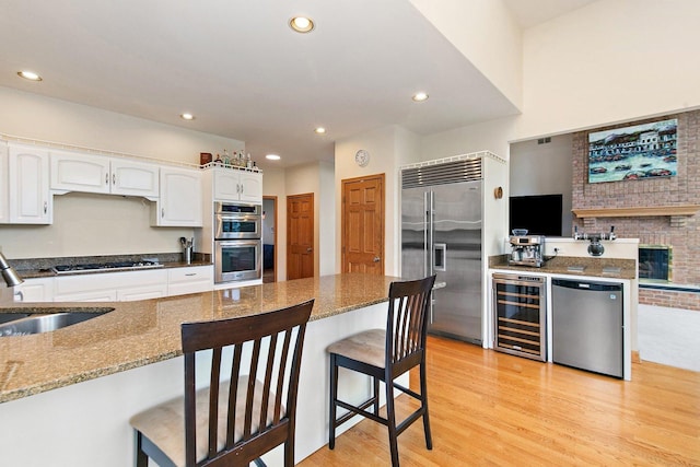 1521 Pendelton Ct, Palatine, IL 60067 - kitchen featuring appliances with stainless steel finishes, wine cooler, dark stone counters, white cabinets, and a breakfast bar