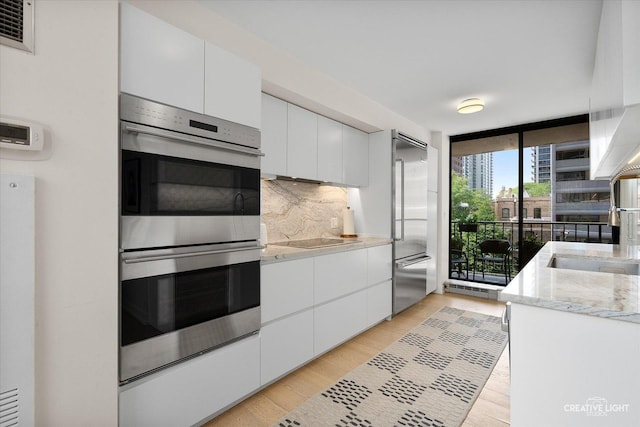 1410 N State Pkwy Unit 5B, Chicago, IL 60610 - kitchen with stainless steel appliances, tasteful backsplash, white cabinetry, light wood-type flooring, and a wall of windows