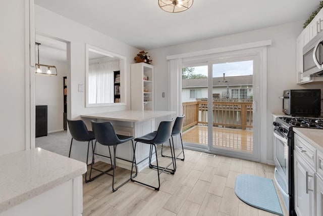 1669 W Bayside Ct, Hoffman Estates, IL 60192 - kitchen featuring appliances with stainless steel finishes, white cabinets, a kitchen bar, light wood-style floors, and light stone countertops