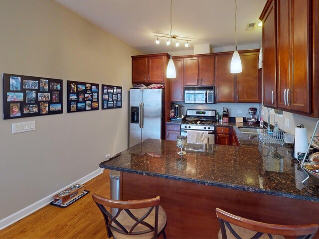 4968 N Milwaukee Ave Unit 2W, Chicago, IL 60630 - kitchen featuring appliances with stainless steel finishes, a peninsula, light wood-type flooring, a breakfast bar area, and dark stone countertops