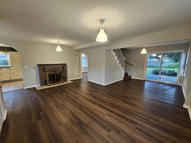 623 Westmoreland Ave, Waukegan, IL 60085 - unfurnished living room featuring arched walkways, stairs, dark wood finished floors, and a stone fireplace