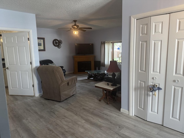 600 W White St, Clinton, IL 61727 - living room featuring a ceiling fan, a fireplace with raised hearth, light wood-style floors, and a textured ceiling