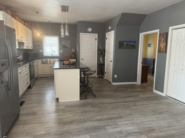 600 W White St, Clinton, IL 61727 - kitchen featuring appliances with stainless steel finishes, a breakfast bar area, wood finished floors, dark countertops, and a center island