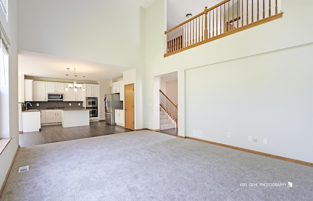 1305 Lilac Ln, Harvard, IL 60033 - unfurnished living room with dark colored carpet, a chandelier, a towering ceiling, and stairs