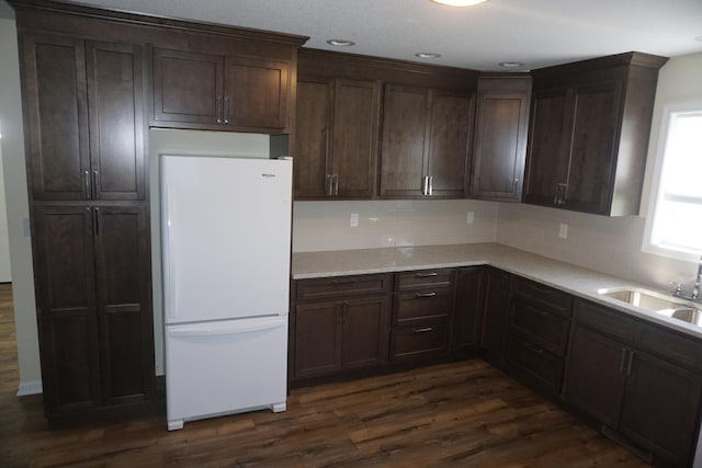 kitchen with freestanding refrigerator, backsplash, dark wood finished floors, light countertops, and dark brown cabinets
